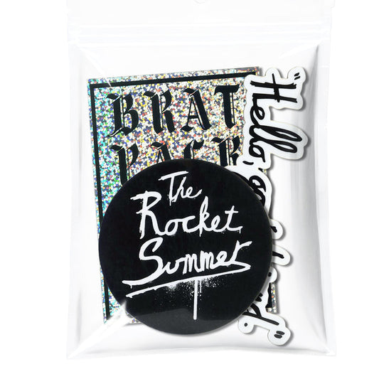 A clear plastic bag featuring three The Rocket Summer stickers: a large round logo in white script, a rectangular holographic Brat Pack sticker, and a white sticker with black cursive text.