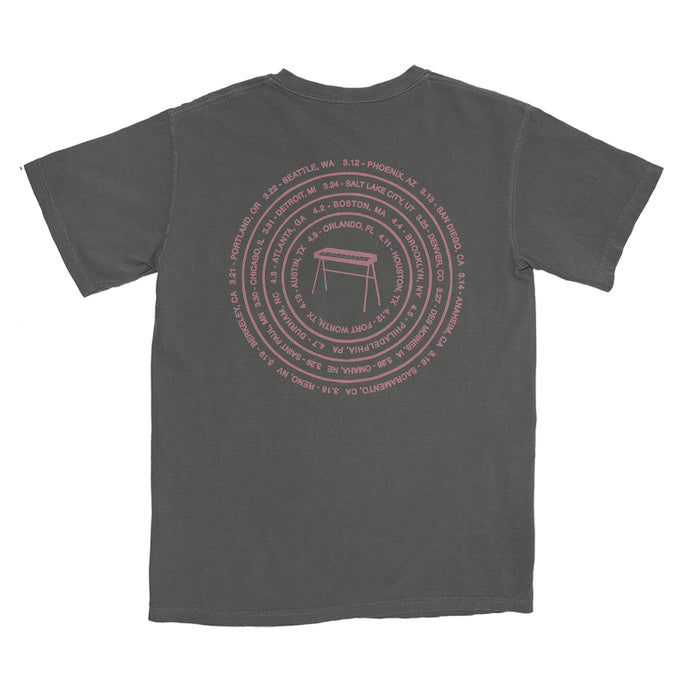 A faded black The Rocket Summer Comfort Colors T-shirt with a pink circular back design of city names and dates around a minimalist table, made from soft, garment-dyed ring-spun cotton for lasting comfort.