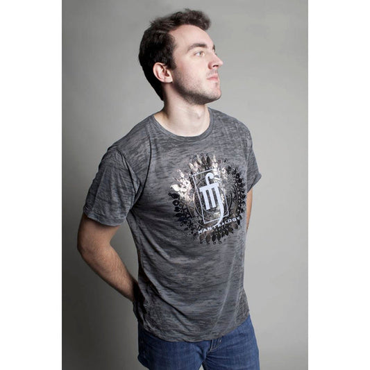 A man wears a gray ultra-soft burnout shirt featuring the Mantralogy logo, standing against a plain light background and gazing slightly upward with his hands behind his back.