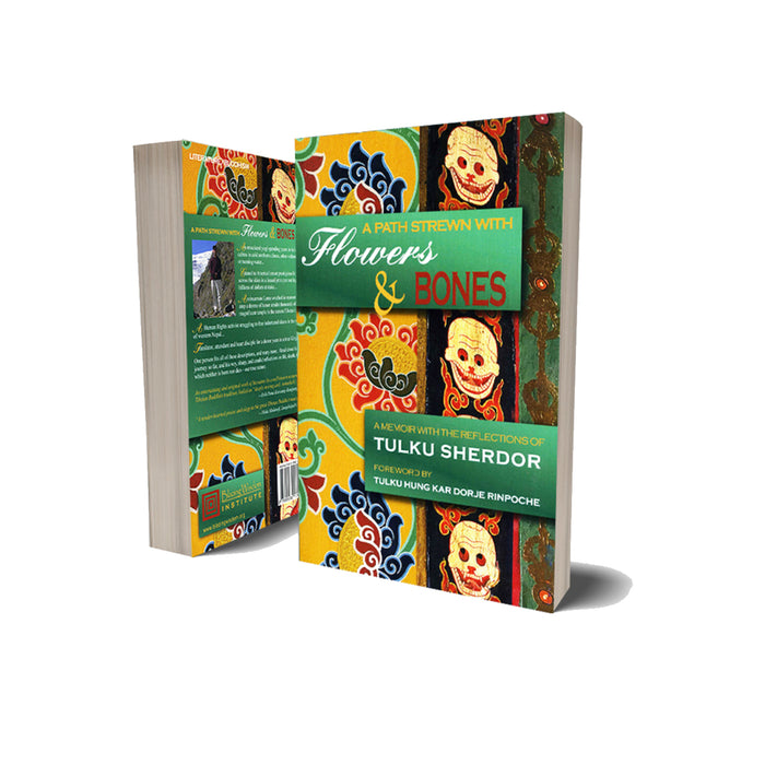 A book from Tibetan Buddhism, titled A Path Strewn with Flowers & Bones by reincarnate Lama Tulku Sherdor, stands upright and slightly open, displaying a vibrant cover with Tibetan-inspired motifs and smiling skulls. Part of the spine is visible.