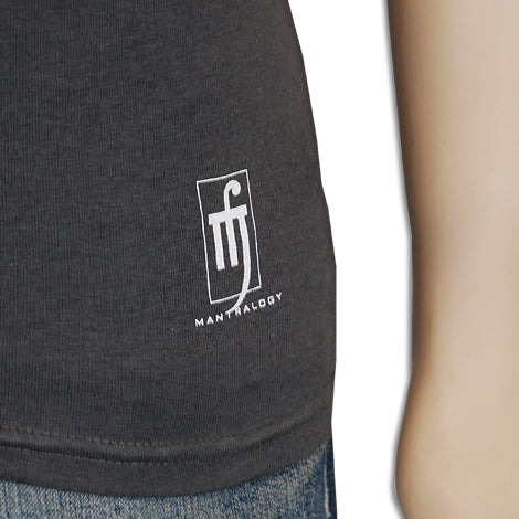 Close-up of the lower side of a dark gray Mantralogy t-shirt with a white logo and stylized design, shown next to a persons arm and blue jeans.
