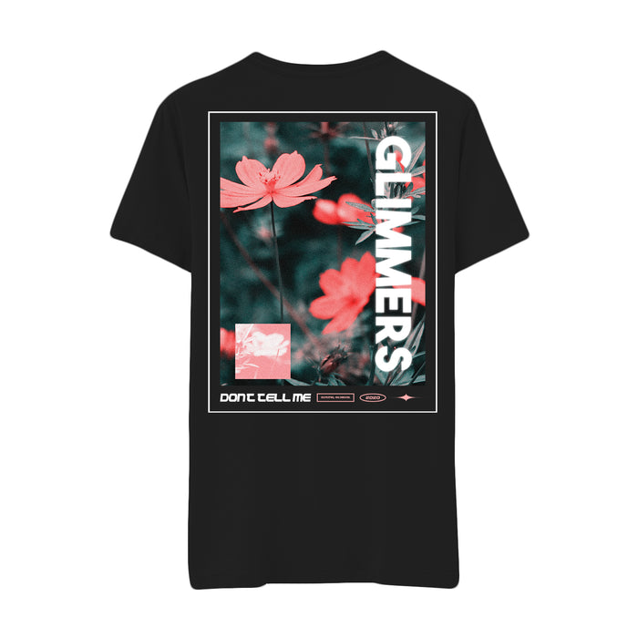 Black glimmers t-shirt featuring a graphic of pink flowers with blurred green foliage. GLIMMERS is printed vertically in bold white letters, with smaller DONT TELL ME text and graphic accents below the flowers.