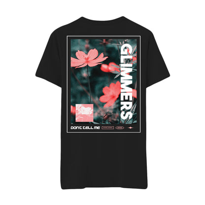 Black glimmers t-shirt featuring a graphic of pink flowers with blurred green foliage. GLIMMERS is printed vertically in bold white letters, with smaller DONT TELL ME text and graphic accents below the flowers.