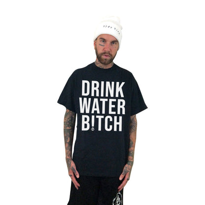 A tattooed man in a white beanie and Stay Sick Clothing’s bold black “DRINK WATER BITCH” tee stands against a white background, confidently promoting hydration with the brand’s unapologetic message.