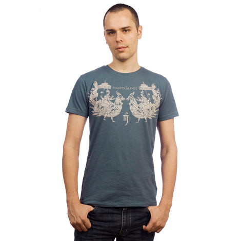 A young man with short hair faces the camera, wearing a Mantralogy blue graphic T-shirt with white designs and dark jeans, set against a plain white background.