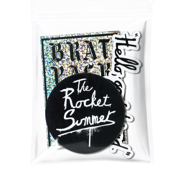 A clear plastic bag featuring three The Rocket Summer stickers: a large round logo in white script, a rectangular holographic Brat Pack sticker, and a white sticker with black cursive text.