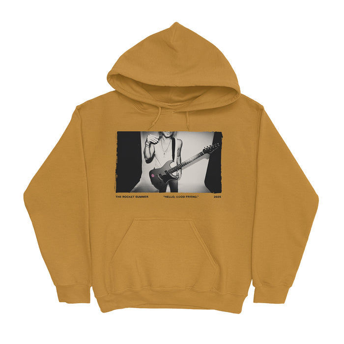 Mustard yellow fleece pullover hoodie by The Rocket Summer, showcasing a black-and-white photo of someone playing an electric guitar with “THE ROCKET SUMMER,” “HELLA GOOD FRIEND,” and “2023” printed below.