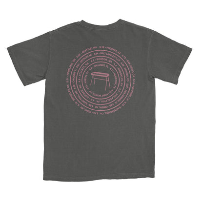 A faded black The Rocket Summer Comfort Colors T-shirt with a pink circular back design of city names and dates around a minimalist table, made from soft, garment-dyed ring-spun cotton for lasting comfort.