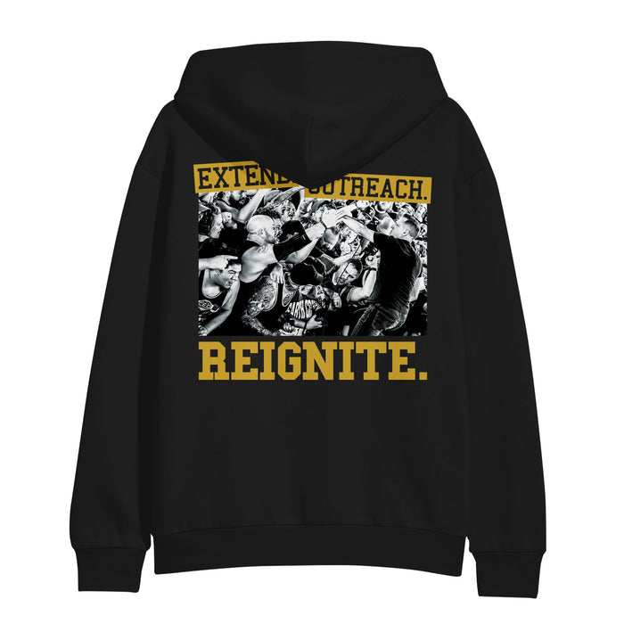 This Shai Hulud black Gildan Heavy Blend pullover hoodie displays a printed black and white concert crowd photo with people cheering. Yellow text above reads EXTENDED OUTREACH; below, bold yellow letters spell REIGNITE.
