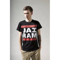 A person stands with hands in pockets, looking down, wearing a Mantralogy unisex t-shirt with JAI RAM in bold white letters on a red and white background, evoking an 80s hip hop vibe against a plain light-colored backdrop.
