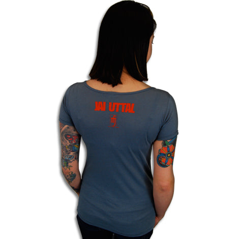 A person with shoulder-length dark hair and colorful arm tattoos is shown from the back, wearing a blue Mantralogy T-shirt with red JAI UTTAL text and a small symbol printed below it.