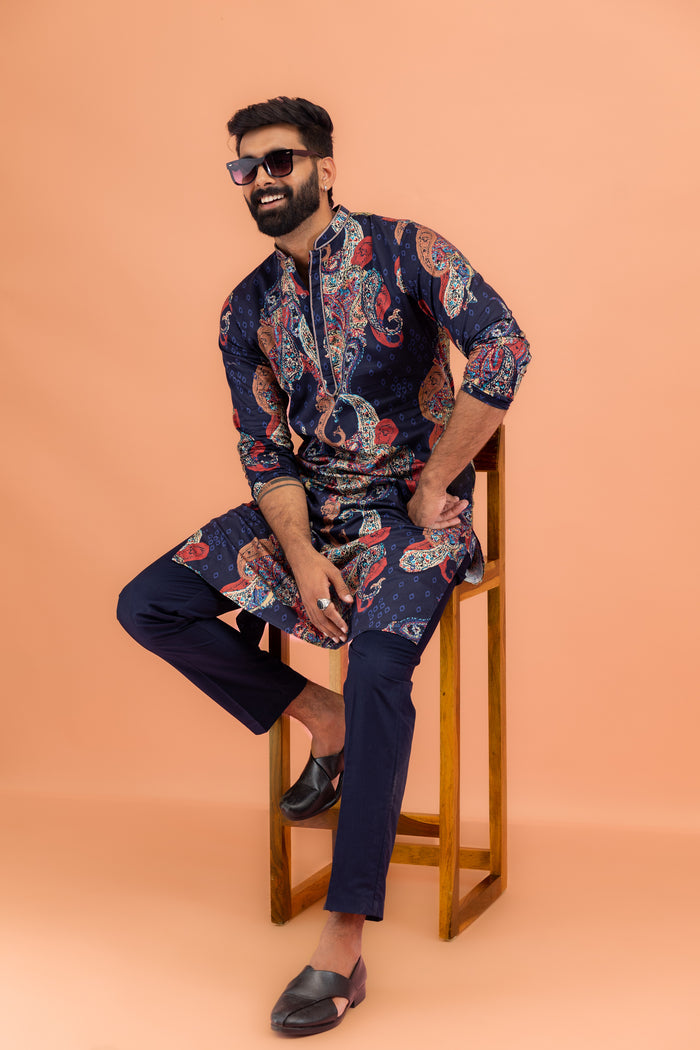 The model is posing confidently on a chair  while wearing Kisah Men’s Navy Blue Kurta Trouser Set