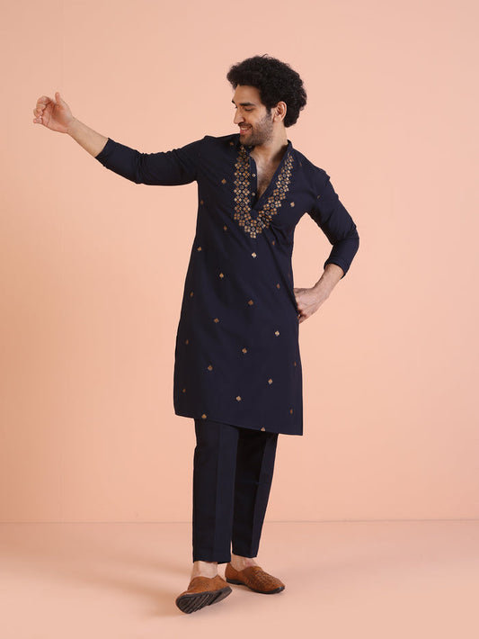 The model is posing with Kisah Men’s Navy Blue Embroidered Kurta Set, pointing sideways in a stylish stance