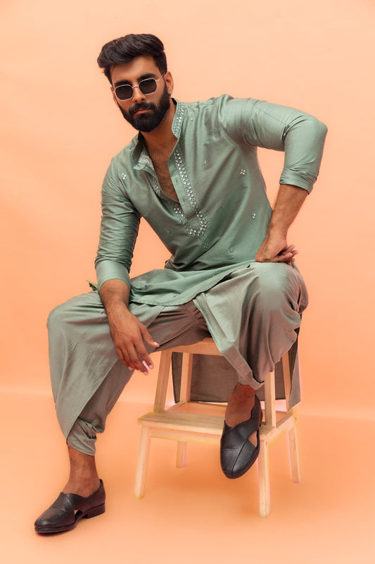 The model is sitting on a chair wearing sunglasses, posing in Kisah Sage Green Mirror Work Kurta with Dhoti set