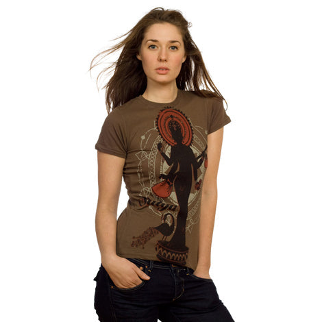 A woman with long brown hair stands with one hand in her pocket, wearing a Mantralogy brown organic cotton t-shirt featuring a large artistic silhouette of a figure with a halo-like design. The background is plain white.