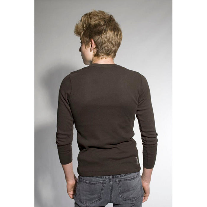 A person with short, light brown hair faces away from the camera, wearing a fitted Mantralogy long-sleeve dark shirt and gray jeans against a plain light background.