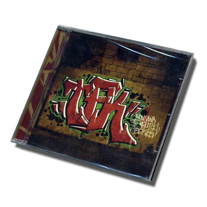 A CD case displays graffiti-style text reading Thousand Foot Krutch Best Of 07-11 on a brick wall. Tilted and shadowed, the cover hints at the bands energetic music within. Brand Name: Thousand Foot Krutch.