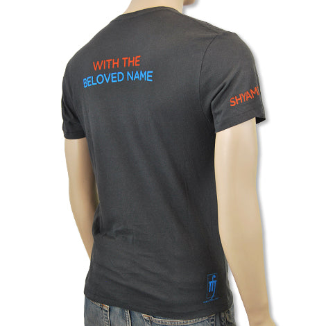 A person wearing a Mantralogy dark gray t-shirt with WITH THE BELOVED NAME on the back and SHYAM in colorful lettering on the left sleeve, shown from behind, paired with blue jeans.