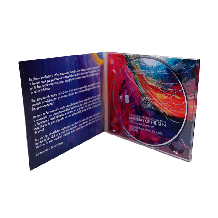 An open CD case displays a colorful booklet on the left with white text and a CD on the right labeled “Mantra Project Volume Two: Mantras of the Sun” by Suzin Green, featuring Surya Namaskar mantras on a vibrant, abstract background.